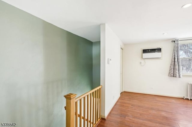 corridor with a wall mounted air conditioner, radiator heating unit, and light hardwood / wood-style flooring