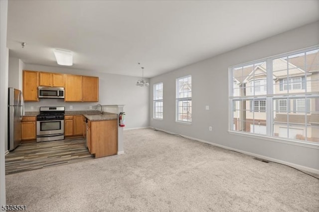 kitchen with sink, appliances with stainless steel finishes, kitchen peninsula, carpet floors, and pendant lighting