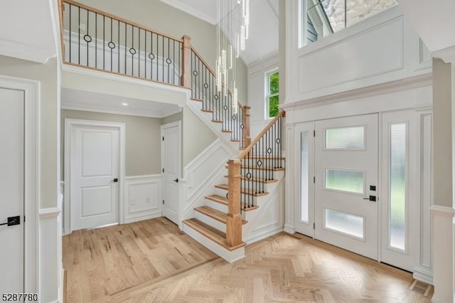 entryway with a towering ceiling, crown molding, and light parquet floors