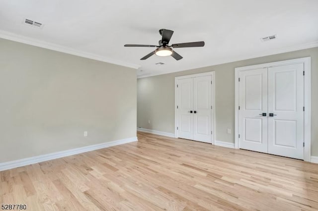 unfurnished bedroom with ceiling fan, light hardwood / wood-style flooring, ornamental molding, and multiple closets