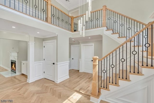 stairway with crown molding, parquet floors, a towering ceiling, a premium fireplace, and decorative columns