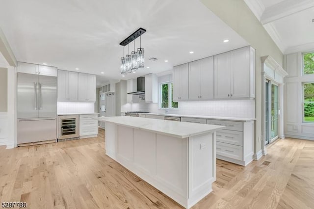 kitchen featuring appliances with stainless steel finishes, white cabinets, wall chimney range hood, beverage cooler, and a kitchen island