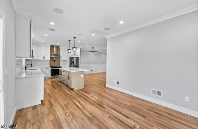 kitchen featuring a kitchen island, appliances with stainless steel finishes, white cabinetry, hanging light fixtures, and wall chimney exhaust hood