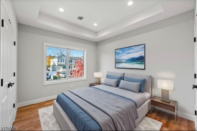 bedroom with light hardwood / wood-style floors and a raised ceiling