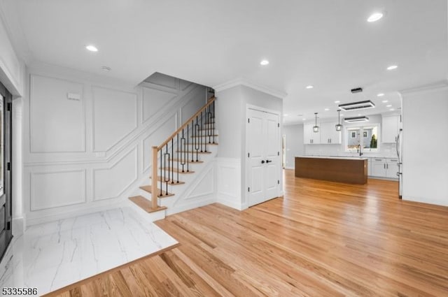 unfurnished living room featuring sink, crown molding, and light hardwood / wood-style flooring