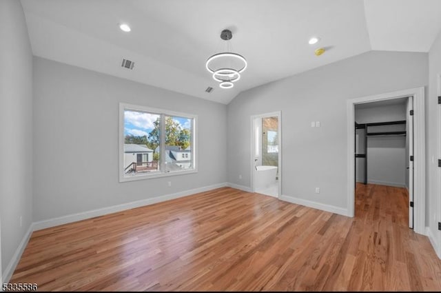 unfurnished bedroom with lofted ceiling, a spacious closet, connected bathroom, and light wood-type flooring