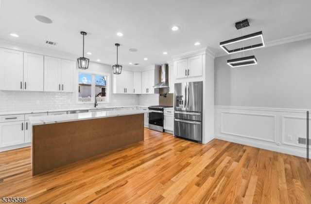 kitchen featuring white cabinetry, pendant lighting, stainless steel appliances, and wall chimney range hood