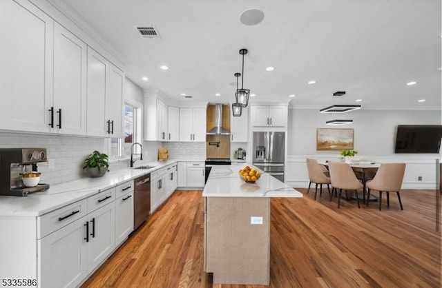 kitchen with sink, white cabinets, a center island, stainless steel appliances, and wall chimney range hood