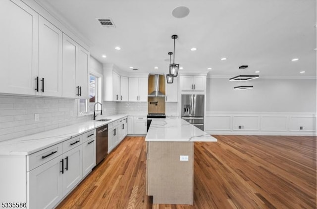 kitchen featuring sink, a center island, appliances with stainless steel finishes, wall chimney range hood, and white cabinets