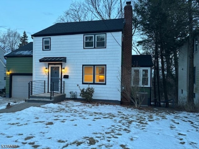 view of front facade featuring a chimney, an attached garage, central AC unit, and a standing seam roof