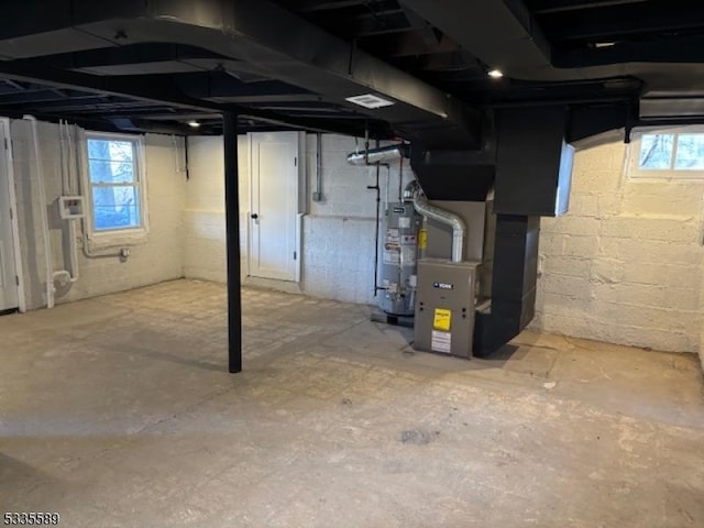 basement with a wealth of natural light, heating unit, and gas water heater