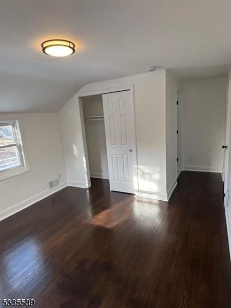 unfurnished bedroom with lofted ceiling, a closet, and dark hardwood / wood-style floors