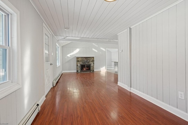 unfurnished living room with a baseboard heating unit, a stone fireplace, a wealth of natural light, and hardwood / wood-style floors