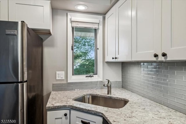 kitchen with stainless steel refrigerator, light stone countertops, sink, and white cabinets