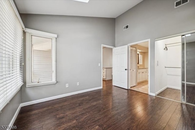 unfurnished bedroom with ensuite bath, dark hardwood / wood-style flooring, high vaulted ceiling, and a closet