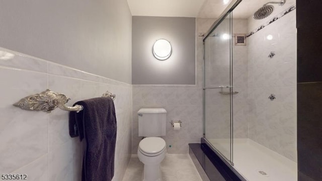 bathroom with tile walls, tile patterned flooring, a shower with door, and toilet