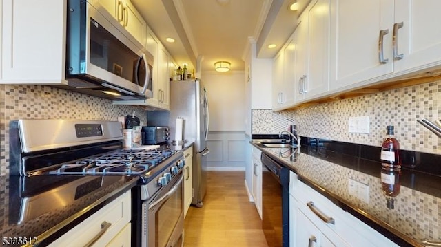 kitchen featuring appliances with stainless steel finishes, white cabinetry, backsplash, light hardwood / wood-style floors, and dark stone counters