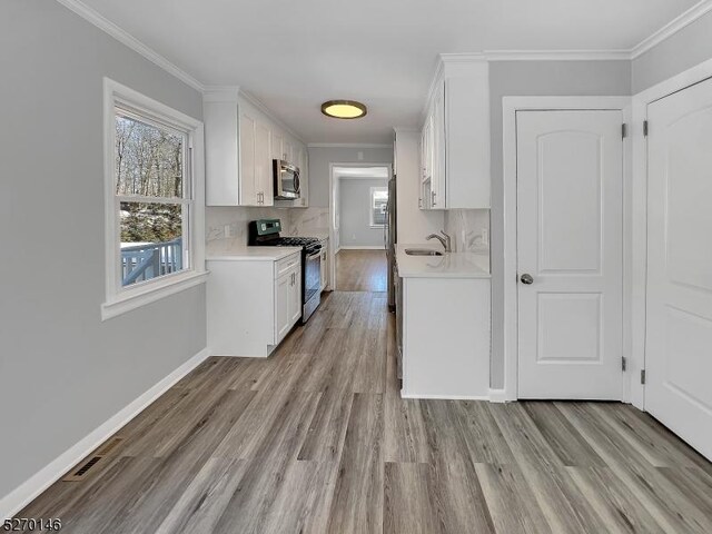 kitchen with white cabinets, backsplash, ornamental molding, stainless steel appliances, and light hardwood / wood-style flooring