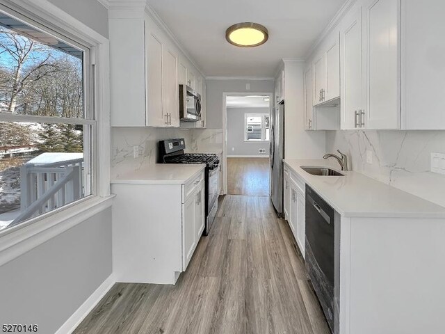 kitchen with sink, white cabinetry, light hardwood / wood-style flooring, stainless steel appliances, and backsplash