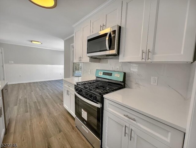 kitchen featuring white cabinetry, stainless steel appliances, ornamental molding, light hardwood / wood-style floors, and decorative backsplash