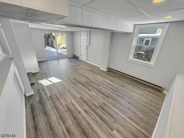 interior space with a drop ceiling, light hardwood / wood-style floors, and baseboard heating