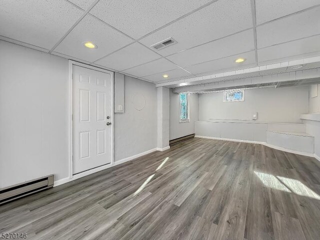 basement with a baseboard heating unit, wood-type flooring, and a paneled ceiling