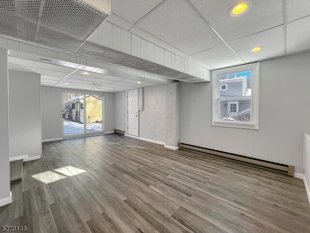 basement featuring a paneled ceiling, wood-type flooring, and a baseboard heating unit