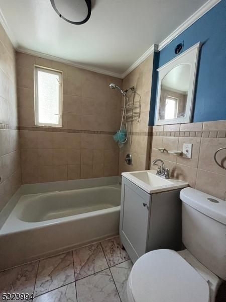 full bathroom with tiled shower / bath, ornamental molding, toilet, and tile walls