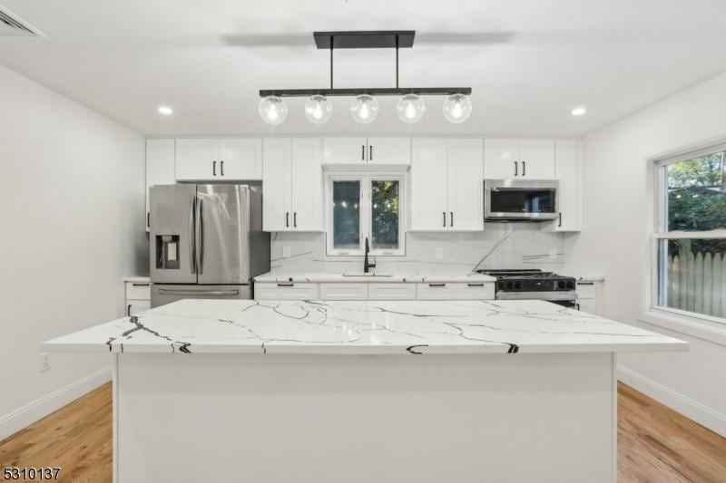 kitchen with a kitchen island, white cabinetry, appliances with stainless steel finishes, and light stone counters