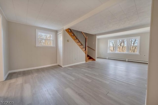 unfurnished room with wood-type flooring, a baseboard heating unit, and a healthy amount of sunlight