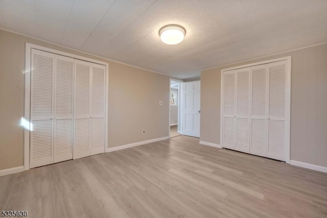 unfurnished bedroom featuring multiple closets and light hardwood / wood-style flooring