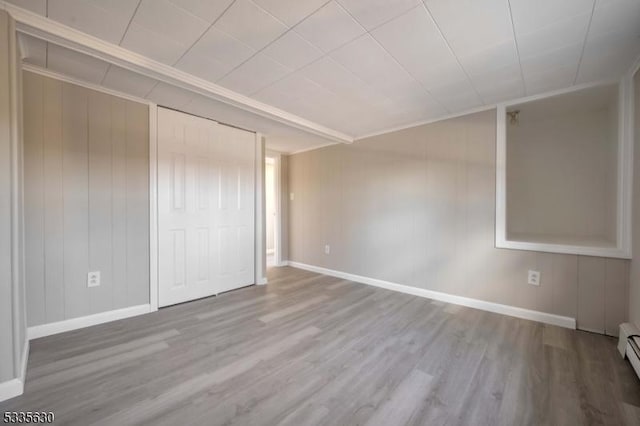 unfurnished bedroom with a baseboard heating unit, light wood-type flooring, and a closet