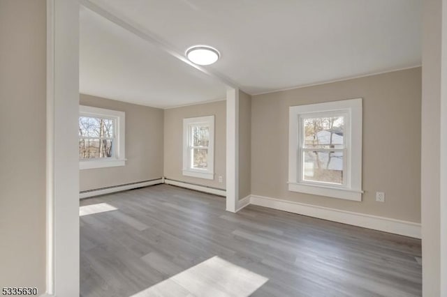 spare room featuring wood-type flooring, a healthy amount of sunlight, and a baseboard radiator