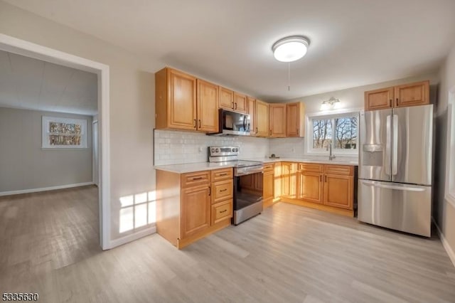 kitchen with appliances with stainless steel finishes, sink, decorative backsplash, and light wood-type flooring