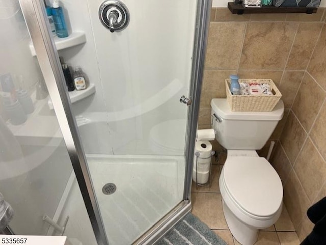 bathroom with toilet, a shower with shower door, tile patterned flooring, and tile walls