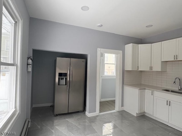 kitchen with sink, stainless steel fridge, baseboard heating, white cabinets, and decorative backsplash