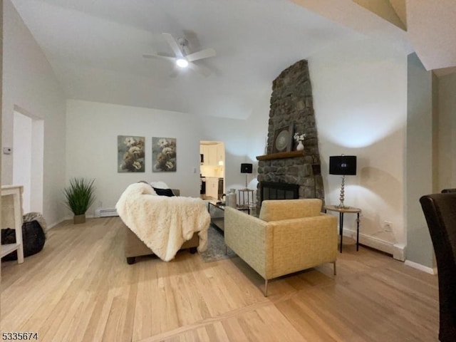 living room featuring baseboards, a ceiling fan, light wood-style flooring, a stone fireplace, and a baseboard heating unit