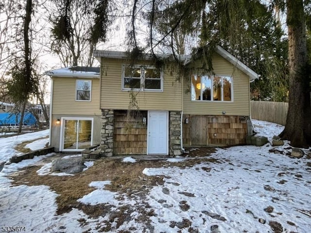 snow covered house featuring stone siding and fence