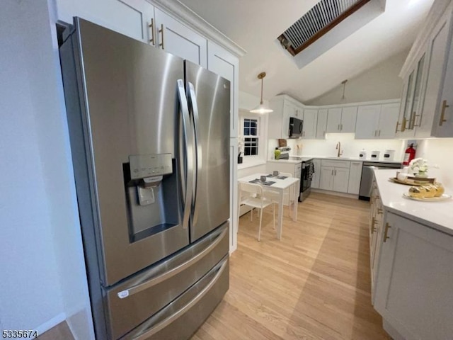 kitchen with lofted ceiling, light countertops, appliances with stainless steel finishes, a sink, and light wood-type flooring