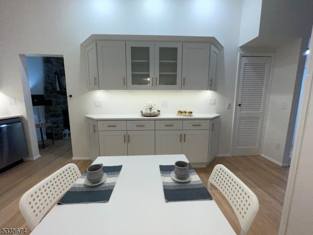 kitchen with light wood-type flooring, glass insert cabinets, light countertops, and gray cabinetry