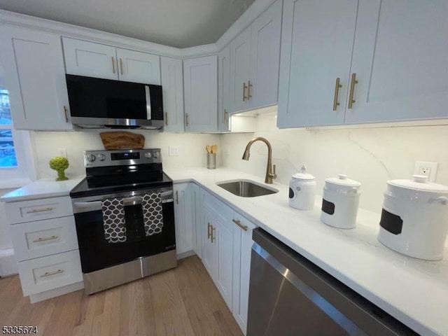 kitchen featuring stainless steel appliances, a sink, light wood-style flooring, and white cabinets