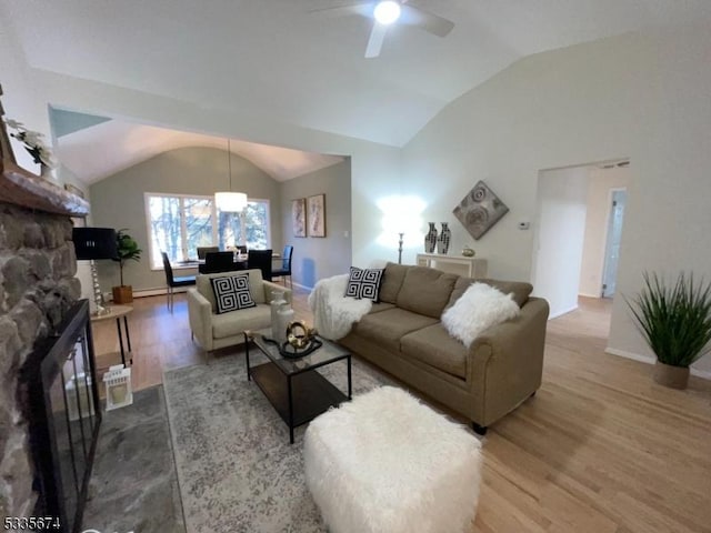 living area with lofted ceiling, ceiling fan, a stone fireplace, and wood finished floors