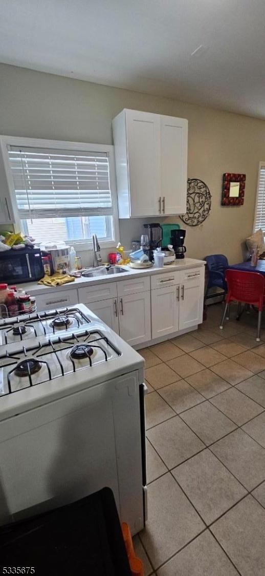 kitchen featuring white cabinetry, white gas range, sink, and light tile patterned floors