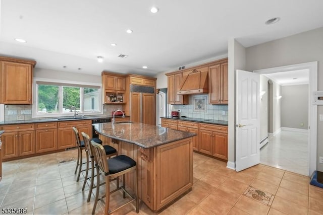 kitchen featuring a center island, sink, custom range hood, and dark stone countertops