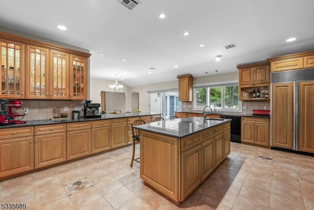 kitchen with hanging light fixtures, paneled built in refrigerator, a kitchen breakfast bar, black dishwasher, and a kitchen island with sink