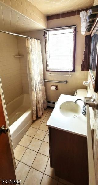 bathroom featuring vanity, tile patterned flooring, a baseboard radiator, and shower / bath combo with shower curtain