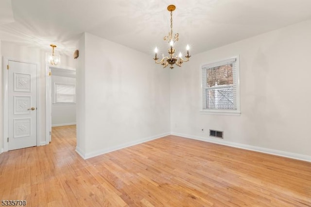 spare room with a notable chandelier and light hardwood / wood-style floors