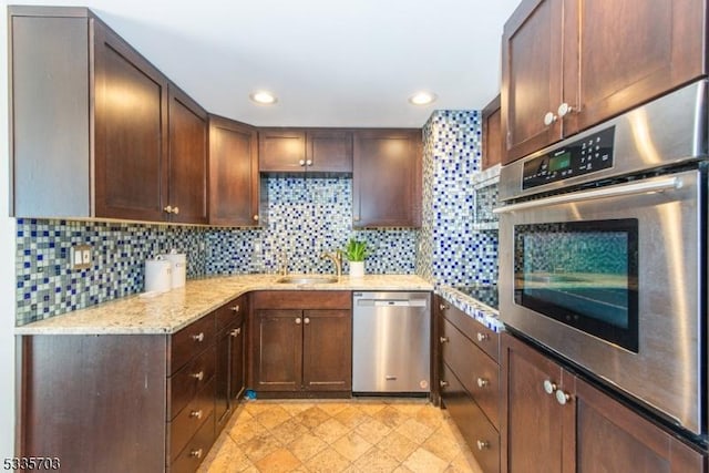 kitchen featuring stainless steel appliances, light stone countertops, sink, and decorative backsplash