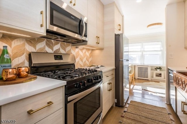 kitchen with light hardwood / wood-style flooring, crown molding, stainless steel appliances, white cabinets, and decorative backsplash