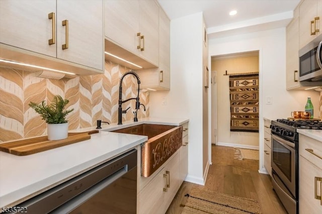 kitchen with light hardwood / wood-style flooring, stainless steel appliances, backsplash, and sink